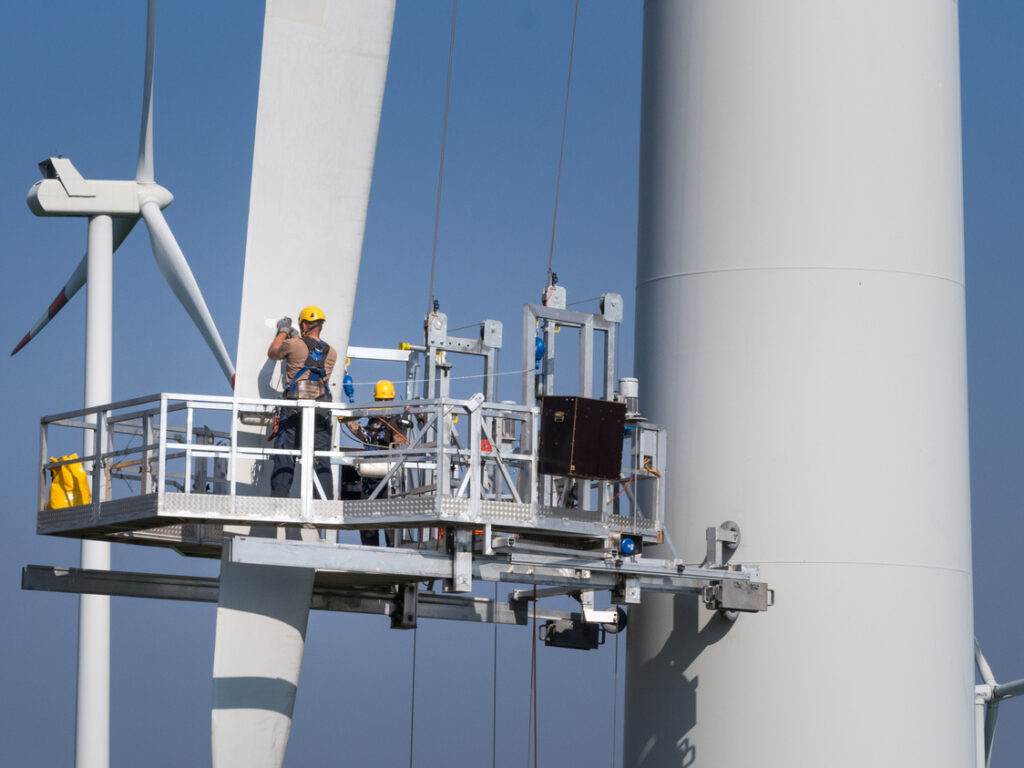 Engineers on a hanging platform servicing a damaged rotor blade on wind turbine